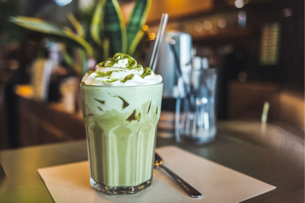 Iced matcha latte toppet med flødeskum og drysset med matcha pulver.