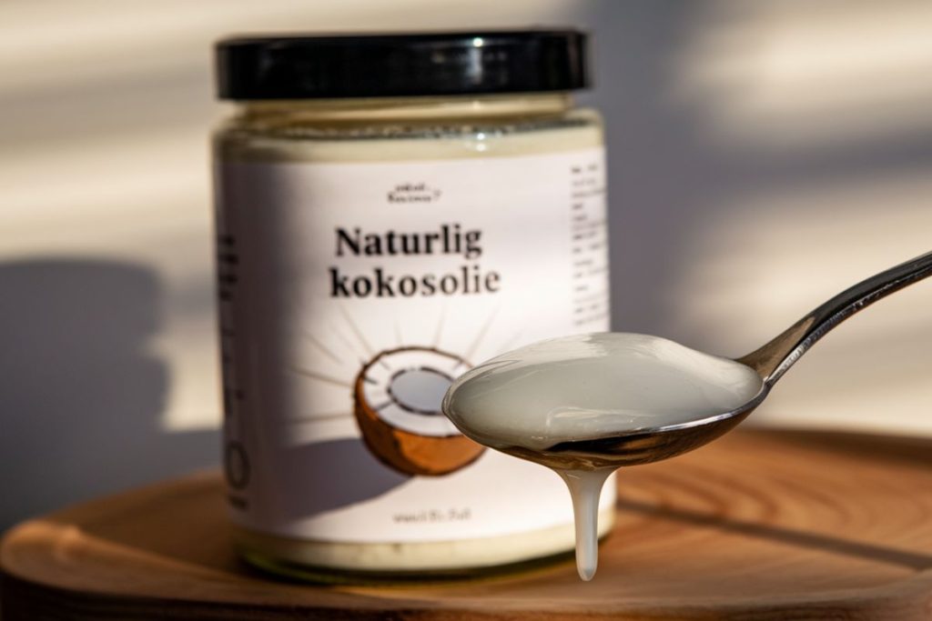 Glas med naturlig kokosolie og en ske med smeltet olie.