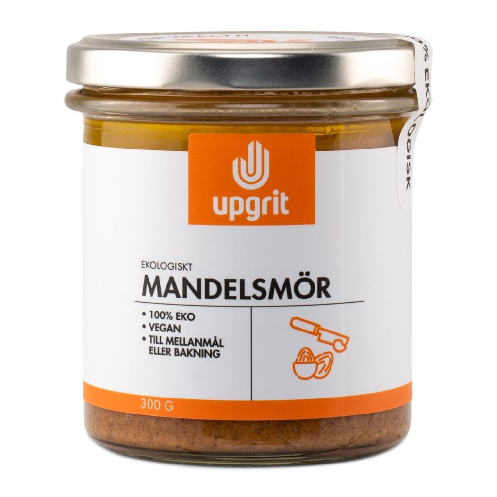 Glas med Upgrit økologisk mandelsmør, tydelig etikette med fokus på økologi og brug i madlavning eller som snack.