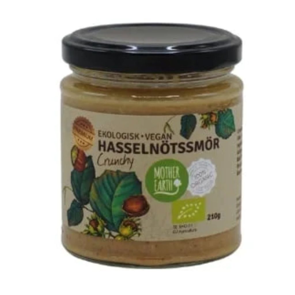 Glas med Mother Earth økologisk crunchy hasselnøddesmør med grønne illustrationer og sort låg.