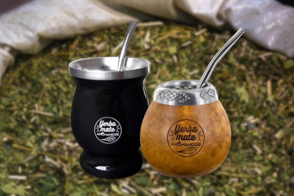 To traditionelle matekopper, en sort og en brun kalabas, begge med sølvkant og metal bombilla sugerør. I baggrunden ses tørret yerba mate te.